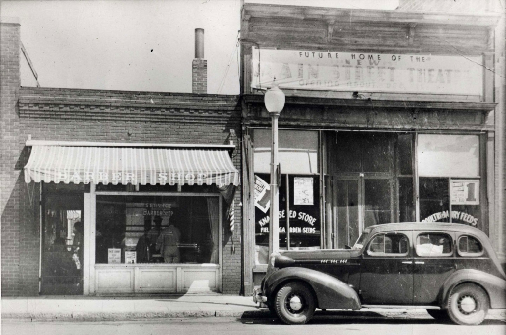 Photo showing car sitting outside of the future Main Street Theatre location in 1938, before it was constructed. A sign above the building entrance reads “Future Home of the new Main Street Theatre.”